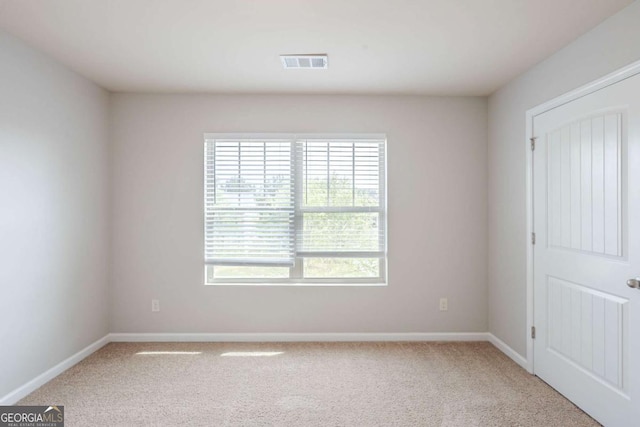 spare room featuring baseboards, light colored carpet, and visible vents