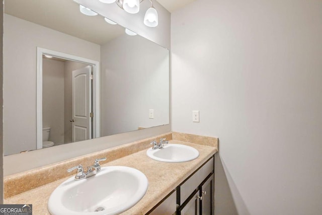 bathroom with a sink, toilet, and double vanity