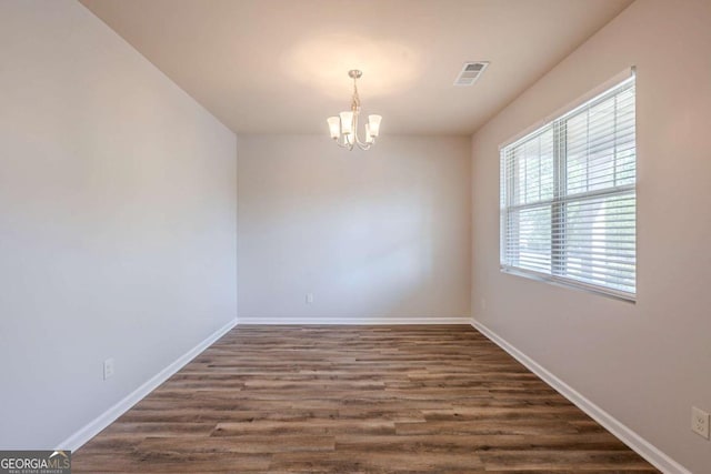 unfurnished room featuring an inviting chandelier, baseboards, visible vents, and dark wood-style floors