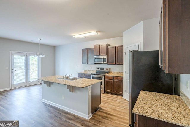 kitchen featuring dark brown cabinetry, a center island with sink, a kitchen bar, light wood finished floors, and stainless steel appliances
