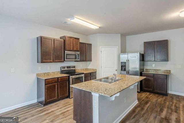 kitchen with baseboards, appliances with stainless steel finishes, a sink, and wood finished floors