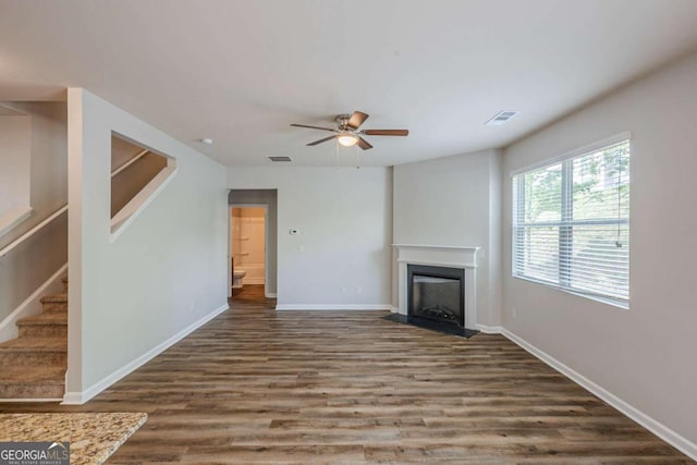 unfurnished living room with a ceiling fan, visible vents, a fireplace, wood finished floors, and stairs