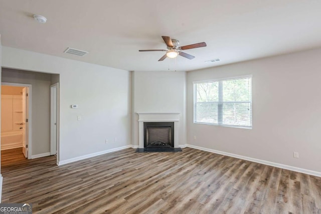unfurnished living room featuring a ceiling fan, visible vents, a fireplace with flush hearth, wood finished floors, and baseboards