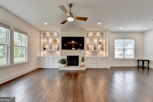 unfurnished living room featuring plenty of natural light, a fireplace, a ceiling fan, and dark wood-style flooring