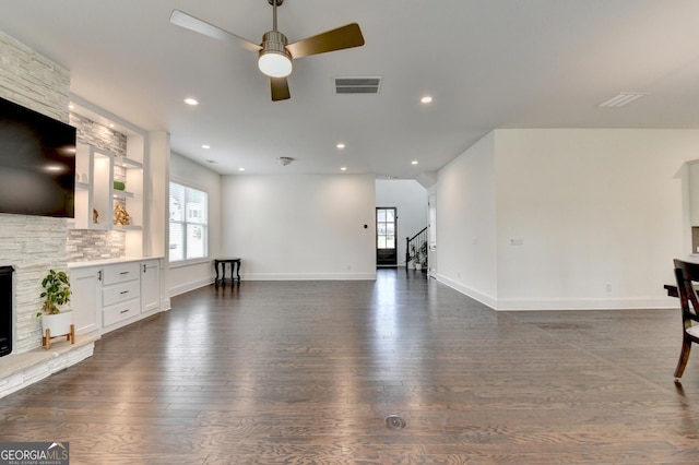 unfurnished living room featuring ceiling fan, visible vents, stairway, and dark wood-type flooring