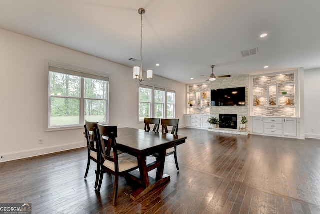 dining room with dark wood-style flooring, visible vents, ceiling fan with notable chandelier, and a fireplace