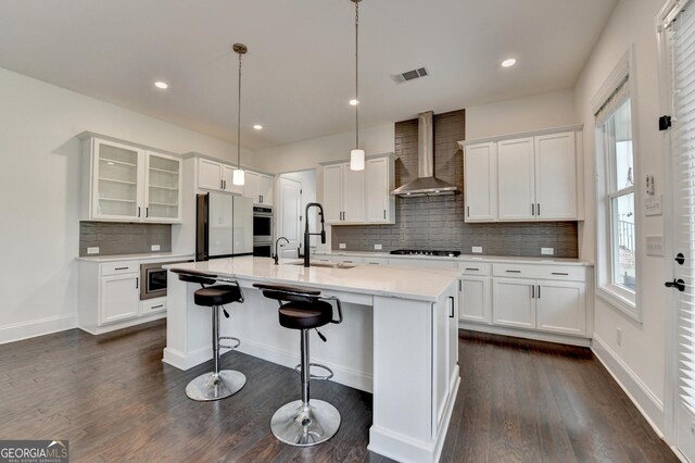 kitchen featuring wall chimney range hood, visible vents, gas stovetop, a sink, and freestanding refrigerator