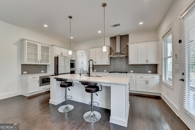 kitchen featuring wall chimney range hood, decorative backsplash, visible vents, appliances with stainless steel finishes, and white cabinets