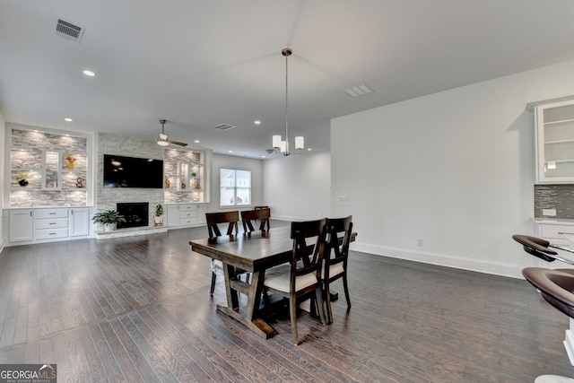 dining room with a stone fireplace, a ceiling fan, dark wood-style flooring, and visible vents