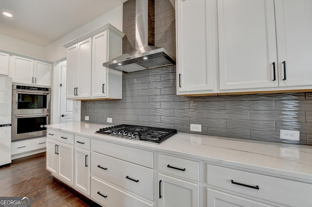 kitchen with backsplash, appliances with stainless steel finishes, white cabinets, wall chimney exhaust hood, and dark wood-type flooring