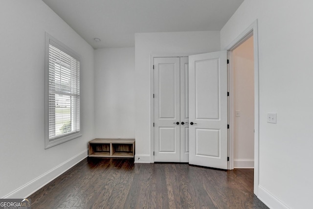 unfurnished bedroom with dark wood-style flooring, baseboards, and a closet