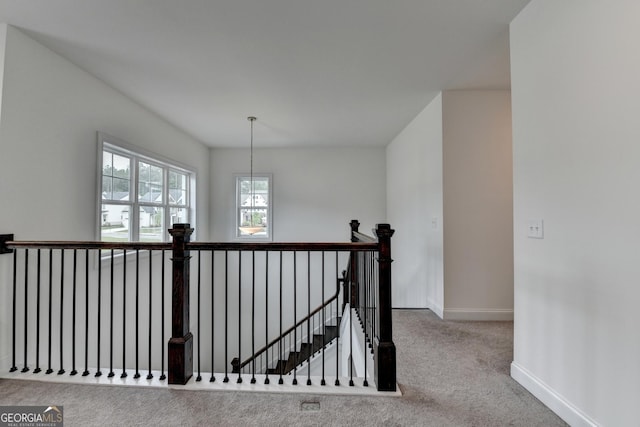 hall with carpet floors, baseboards, and an upstairs landing