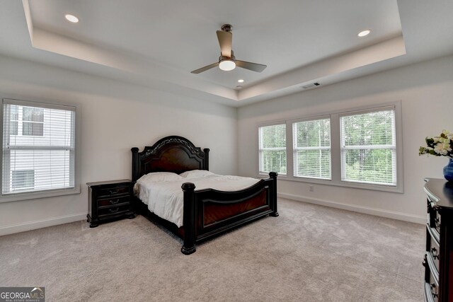 bedroom with a tray ceiling, visible vents, light carpet, and baseboards