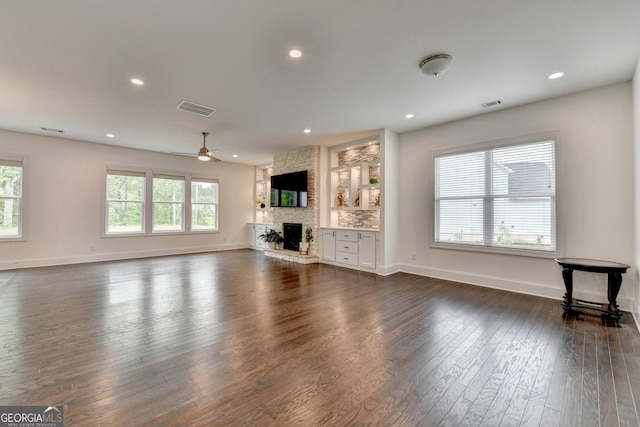 unfurnished living room with visible vents, dark wood-style flooring, ceiling fan, and a stone fireplace