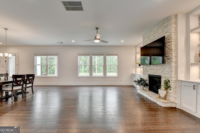 living area featuring dark wood-style flooring, ceiling fan, a stone fireplace, baseboards, and visible vents