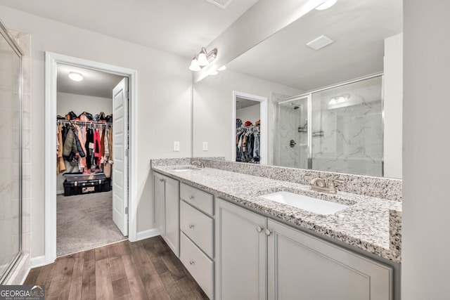 full bath with a sink, double vanity, baseboards, wood finished floors, and a stall shower