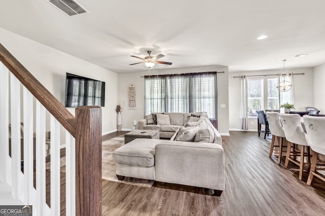 living room with dark wood finished floors, ceiling fan with notable chandelier, baseboards, visible vents, and stairway