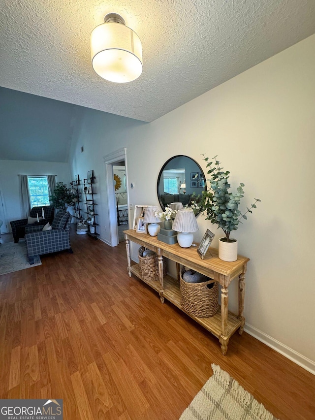 hall with wood finished floors, a textured ceiling, vaulted ceiling, and baseboards