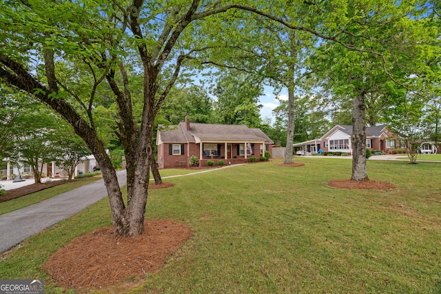 ranch-style house featuring a porch, driveway, a chimney, brick siding, and a front lawn
