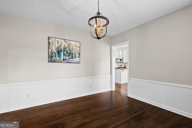 unfurnished dining area with wood finished floors, a wainscoted wall, and a notable chandelier