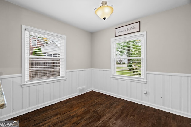 spare room with dark wood finished floors, visible vents, and a wainscoted wall