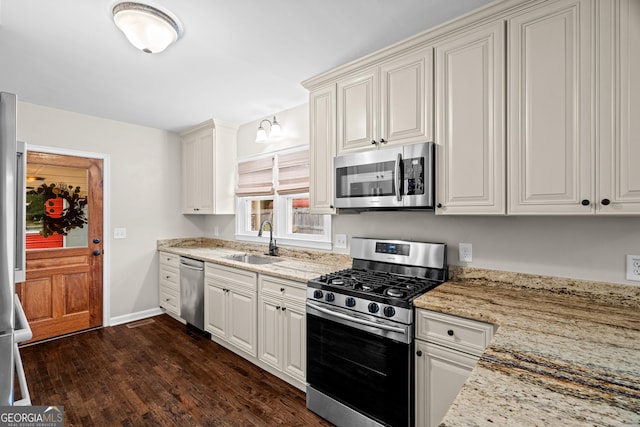 kitchen featuring light stone counters, a sink, stainless steel appliances, baseboards, and dark wood-type flooring