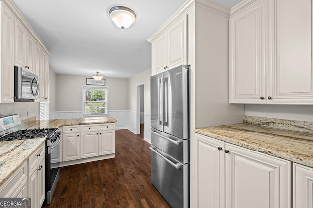 kitchen featuring dark wood-style floors, a wainscoted wall, white cabinets, light stone counters, and appliances with stainless steel finishes