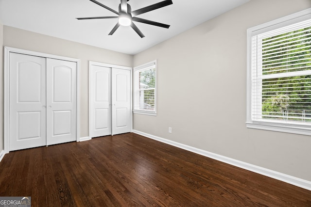 unfurnished bedroom with baseboards, ceiling fan, two closets, and dark wood finished floors