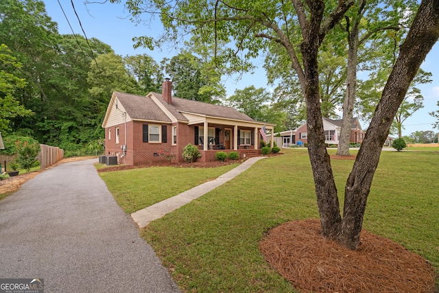 bungalow with brick siding, a porch, a front yard, a chimney, and central air condition unit