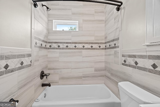 bathroom with bathing tub / shower combination, toilet, and tile walls
