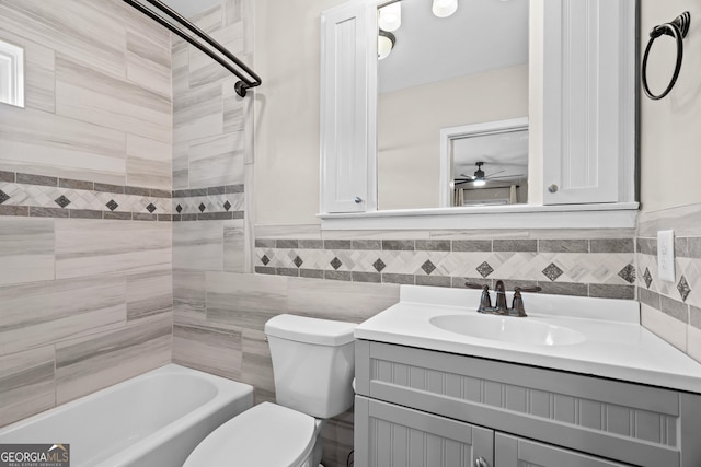bathroom featuring vanity, wainscoting, bathing tub / shower combination, toilet, and tile walls