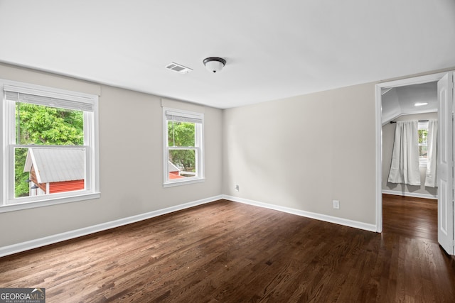 unfurnished room with visible vents, plenty of natural light, baseboards, and dark wood-type flooring