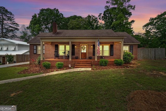 view of front facade featuring fence, covered porch, a front yard, and brick siding