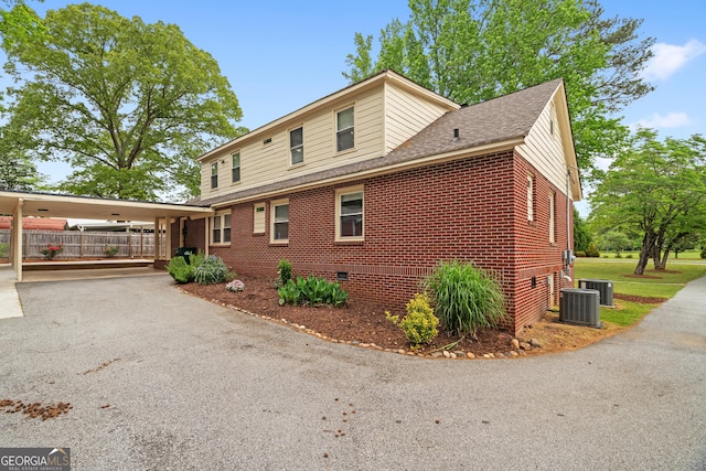 view of home's exterior with crawl space, roof with shingles, brick siding, central AC, and aphalt driveway