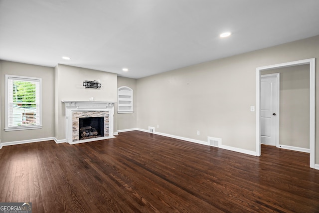 unfurnished living room featuring baseboards, visible vents, a fireplace with flush hearth, and wood finished floors