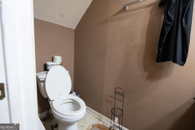 bathroom with baseboards, a textured ceiling, lofted ceiling, and toilet