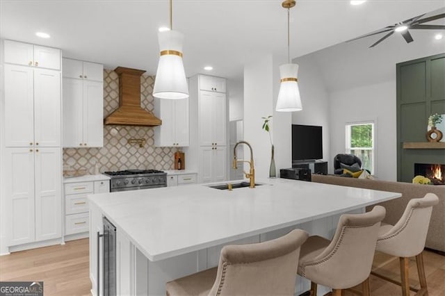kitchen featuring a sink, premium range hood, beverage cooler, open floor plan, and light wood-style flooring