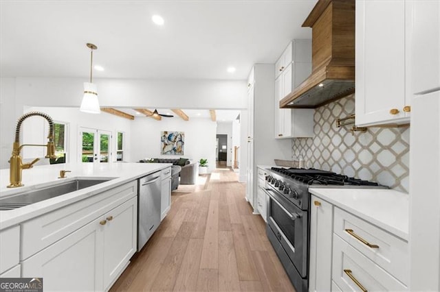 kitchen with wall chimney range hood, a sink, light wood-style flooring, stainless steel appliances, and decorative backsplash