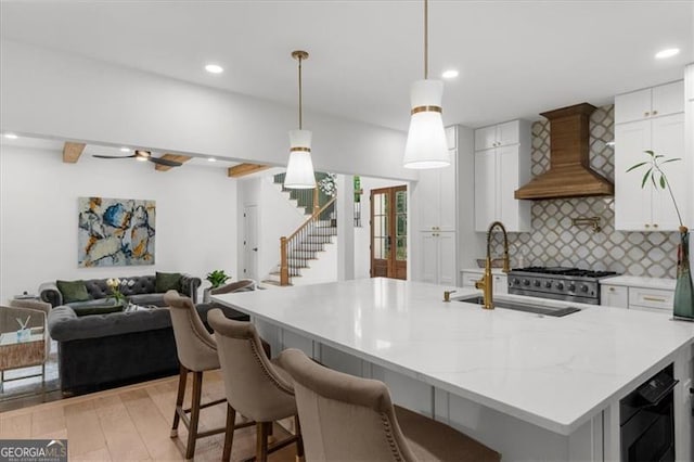 kitchen featuring backsplash, a sink, custom exhaust hood, open floor plan, and white cabinetry