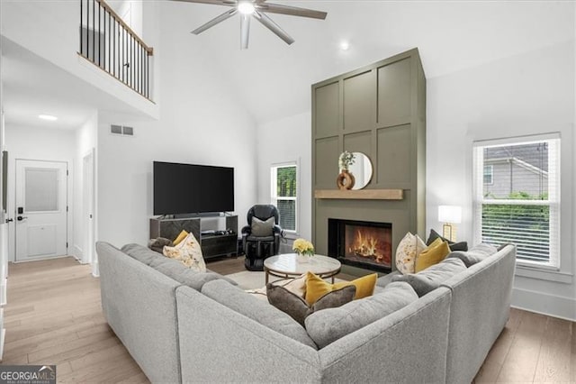 living room featuring visible vents, high vaulted ceiling, a ceiling fan, light wood-type flooring, and a lit fireplace
