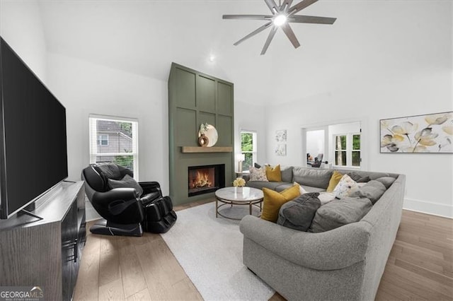 living area with high vaulted ceiling, a ceiling fan, a large fireplace, and wood finished floors