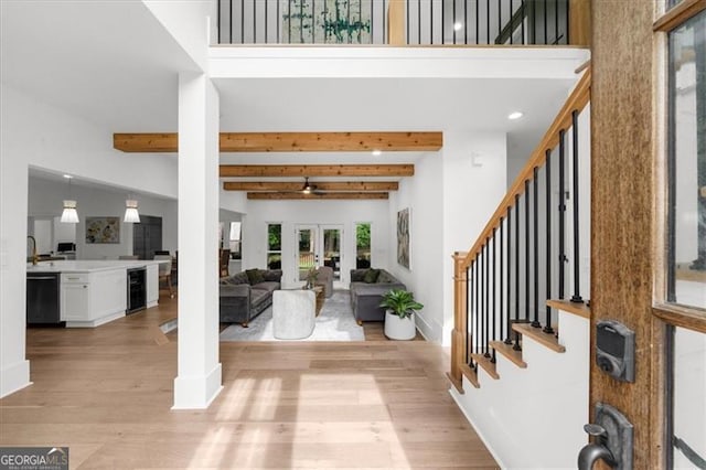 foyer featuring stairs, a towering ceiling, wine cooler, beam ceiling, and light wood-type flooring