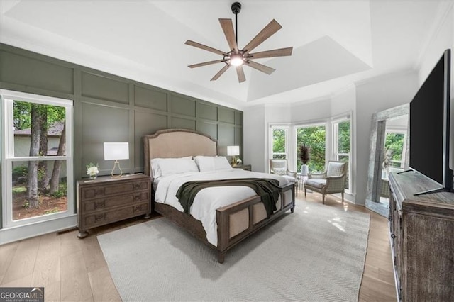bedroom featuring a ceiling fan, a tray ceiling, light wood-type flooring, and a decorative wall