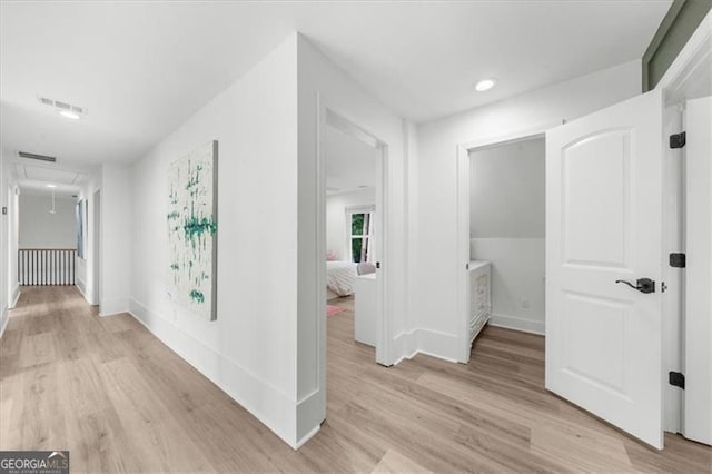 hall featuring baseboards, visible vents, attic access, and light wood-style floors