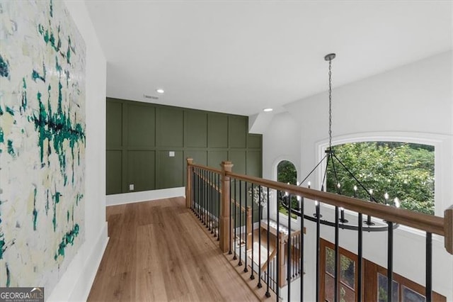 corridor featuring an upstairs landing, wood finished floors, a chandelier, a decorative wall, and recessed lighting