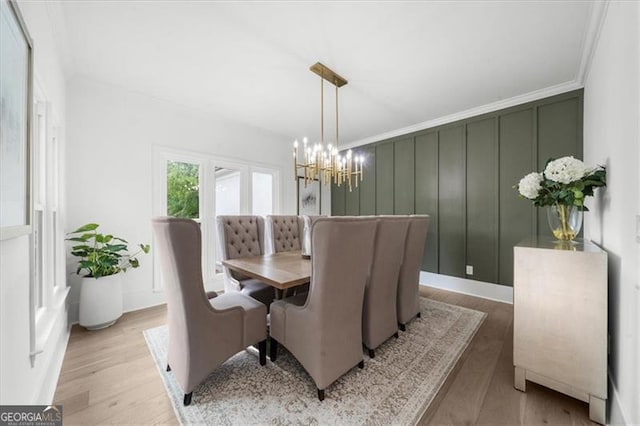 dining space with an inviting chandelier, crown molding, a decorative wall, and wood finished floors