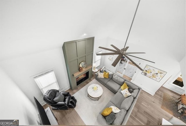 living room with a ceiling fan, a towering ceiling, wood finished floors, and a lit fireplace