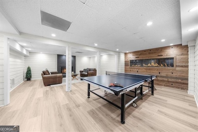 rec room with recessed lighting, wood finished floors, wooden walls, and a lit fireplace