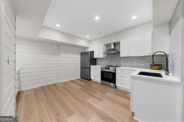 kitchen with freestanding refrigerator, wall chimney exhaust hood, white cabinetry, a sink, and stainless steel range with electric cooktop