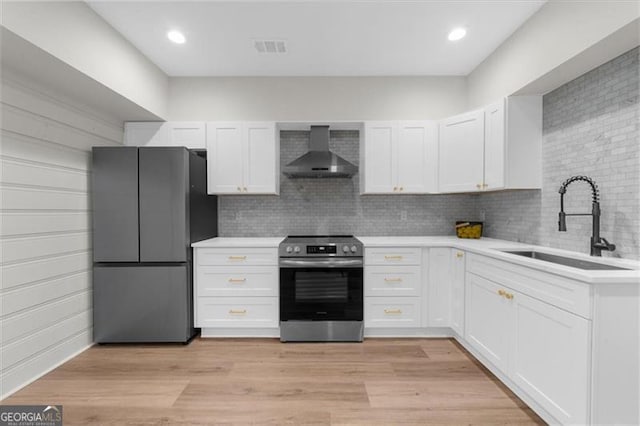 kitchen with wall chimney range hood, stainless steel appliances, a sink, and light countertops
